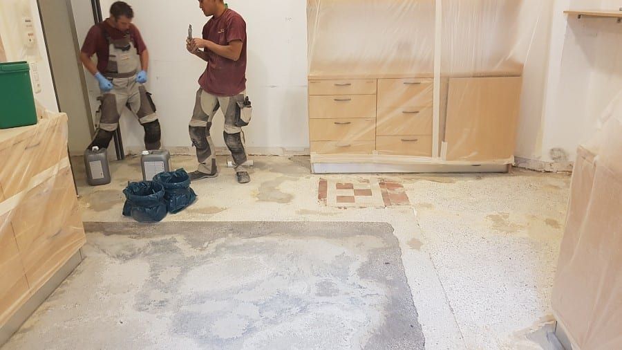 Neue Bodenbeschichtung, schichtweiser Aufbau — Handwerker beim Anrühren der Masse auf dem freigelegten Estrich