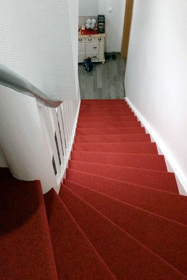 Holztreppe mit rotem Textilbelag — Blick von oben auf den roten Lauf und den Antritt im Flur