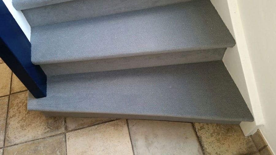 Holztreppe mit hochwertigem Textilbelag — die Antrittsstufen aus der Nähe über dem Fliesenboden